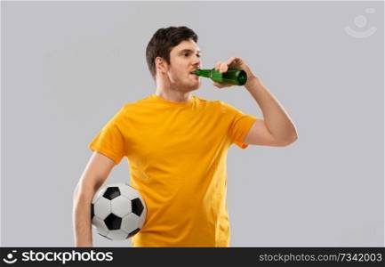 sport, leisure games and people - happy man or football fan in yellow t-shirt with soccer ball drinking beer over grey background. man or football fan with soccer ball drinking beer