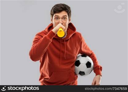 sport, leisure games and people - happy man or football fan in red hoodie with soccer ball blowing vuvuzela horn over grey background. football fan with soccer ball blowing horn