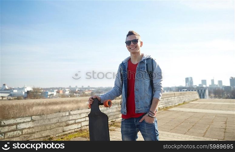 sport, leisure, people and teenage concept - smiling young man or teenager with longboard on city street