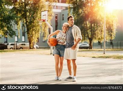sport, love and people concept - happy young couple with ball hugging on basketball playground. happy couple with ball on basketball playground