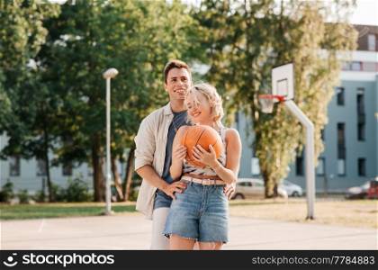sport, love and people concept - happy young couple with ball on basketball playground. happy couple with ball on basketball playground