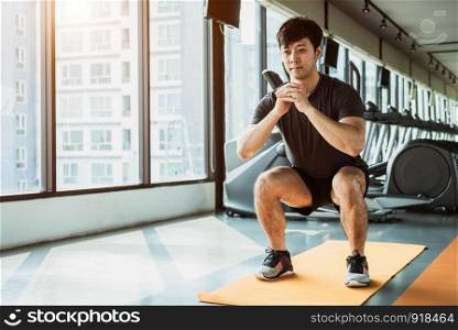 Sport man doing squat posture on yoga mat in fitness gym at condominium in urban. People lifestyles and Sport workout concept.