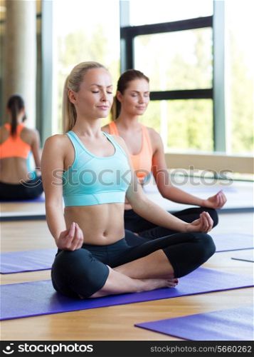 sport, meditation and lifestyle concept - smiling women meditating on mat in gym