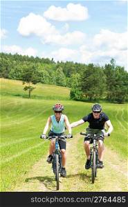 Sport mountain biking - man pushing young girl uphill sunny countryside
