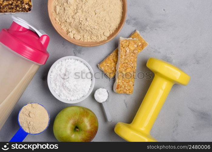 Sport nutrition with vegetarian protein powder and creatine with snacks and dumbbell on concrete background top view flat lay