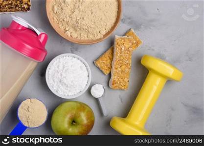 Sport nutrition with vegetarian protein powder and creatine with snacks and dumbbell on concrete background top view flat lay