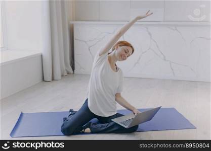 Sport online at home. Young happy caucasian woman with laptop practicing yoga in front of camera. Internet fitness tutorial. Concept of home classes and healthy lifestyle on quarantine.. Young happy woman with laptop practicing yoga in front of camera. Sport online at home.