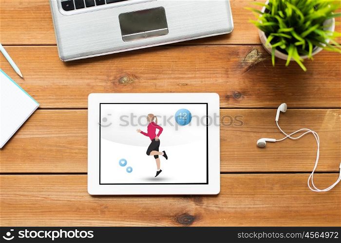 sport, people and technology concept - close up of tablet pc computer with fitness application on screen, laptop and earphones on wooden table