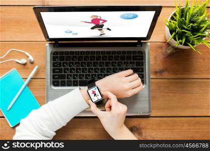 sport, people and technology concept - close up of woman setting smart watch with fitness application on screen and laptop computer on wooden table