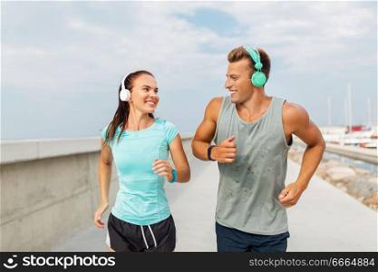 sport, people and technology concept - happy couple with headphones and fitness trackers running outdoors. couple with headphones running outdoors