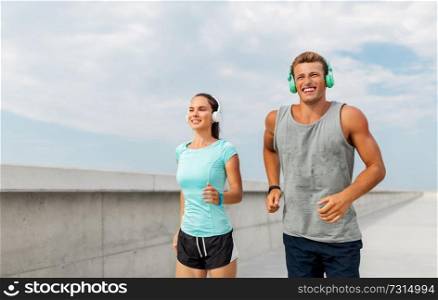 sport, people and technology concept - happy couple with headphones and fitness trackers running outdoors. couple with headphones running outdoors