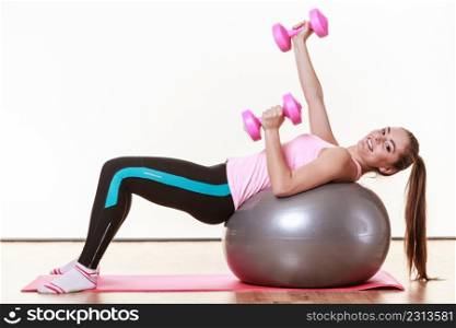 Sport, people, fitness, gym concept. Lady lying on the fit ball. Girl has pink dumbbells.. Lady lying on the fit ball.