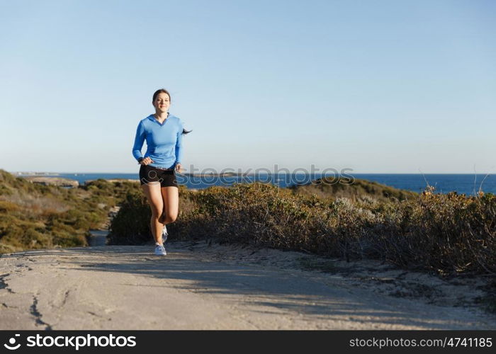 Sport runner jogging on beach working out. Fit female fitness model jogging along ocean