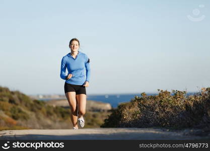 Sport runner jogging on beach working out. Fit female fitness model jogging along ocean