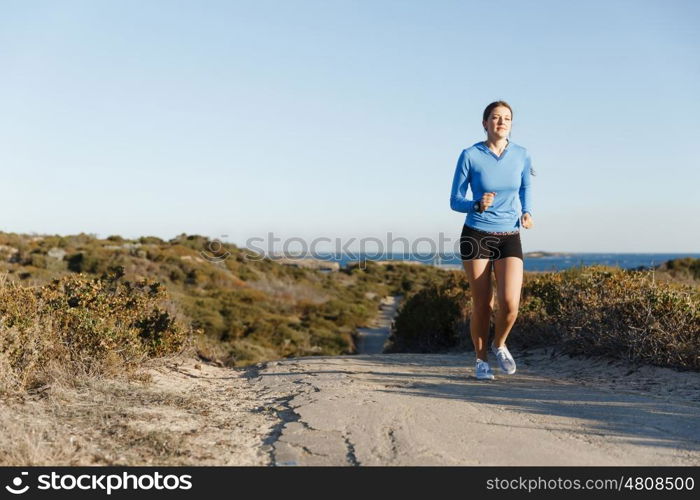 Sport runner jogging on beach working out. Fit female fitness model jogging along ocean