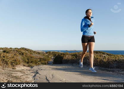 Sport runner jogging on beach working out. Fit female fitness model jogging along ocean