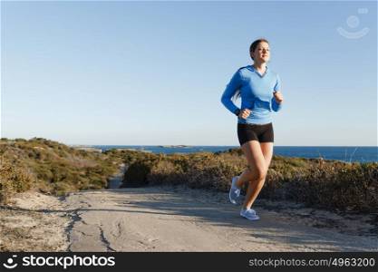Sport runner jogging on beach working out. Fit female fitness model jogging along ocean