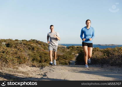 Sport runner jogging on beach working out with her partner. Fit female fitness model jogging along ocean with her partner