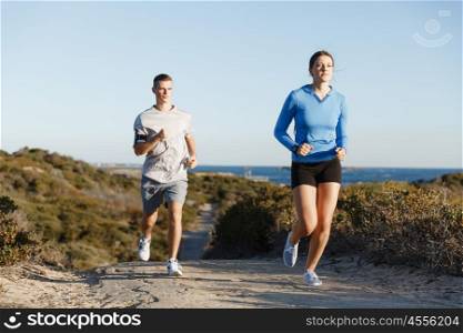 Sport runner jogging on beach working out with her partner. Fit female fitness model jogging along ocean with her partner