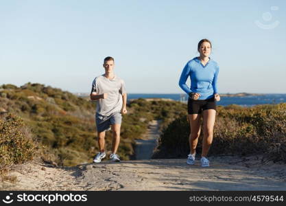 Sport runner jogging on beach working out with her partner. Fit female fitness model jogging along ocean with her partner