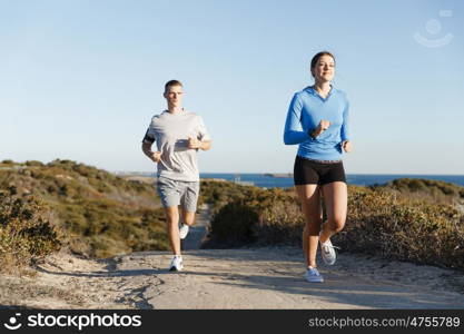 Sport runner jogging on beach working out with her partner. Fit female fitness model jogging along ocean with her partner