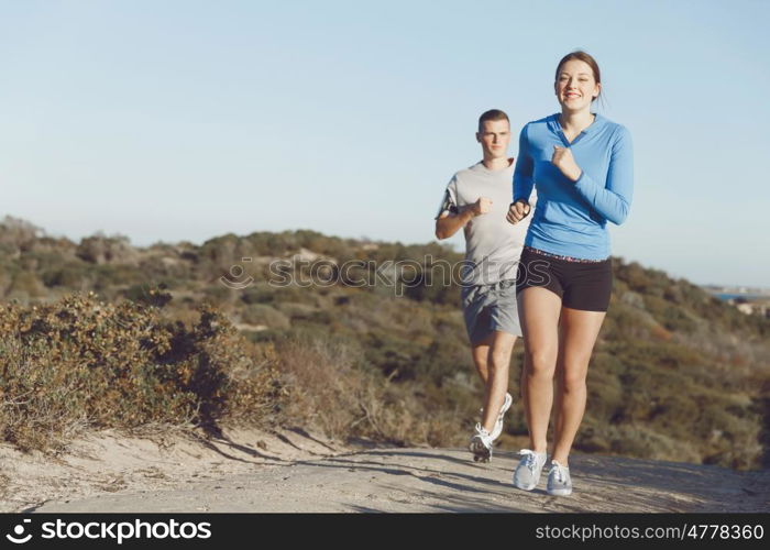 Sport runner jogging on beach working out with her partner. Fit female fitness model jogging along ocean with her partner