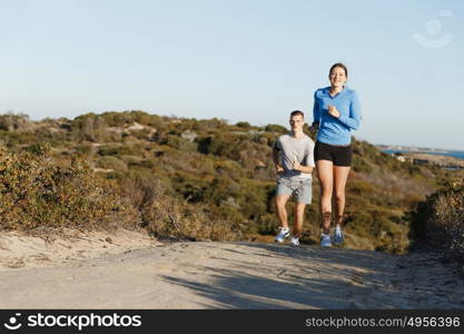 Sport runner jogging on beach working out with her partner. Fit female fitness model jogging along ocean with her partner