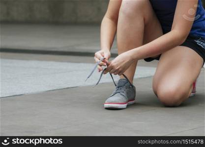 Sport sneakers footwear young woman knelt down do up shoelaces. Ready running shoes in sport exercise jogging person. Close up hands tie up runner shoelaces in fitness gym healthy person lifestyle.