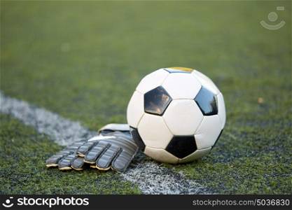 sport, soccer and game - ball and goalkeeper gloves on football field. soccer ball and goalkeeper gloves on field