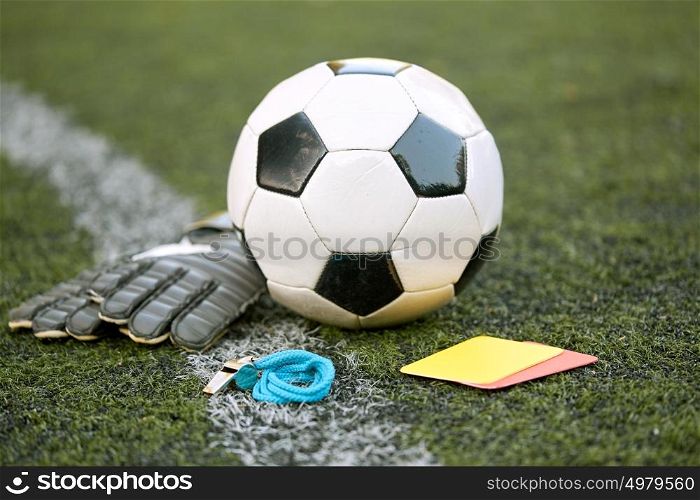 sport, soccer and game - ball, goalkeeper gloves, referee whistle and caution card on football field. ball, gloves, whistle and cards on soccer field