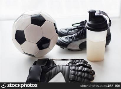 sport, soccer and sports equipment concept - close up of ball, football boots, goalkeeper gloves and protein shake bottle with drink
