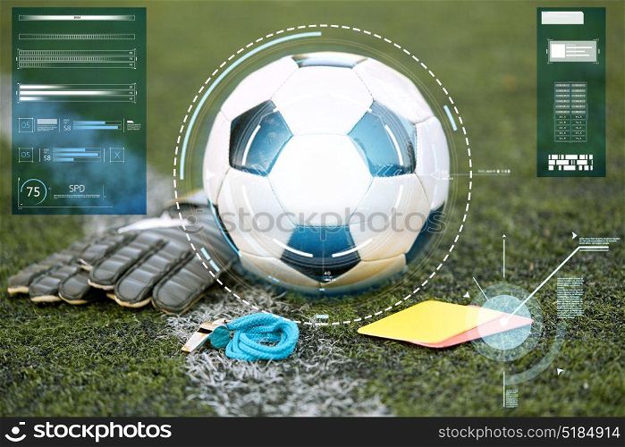 sport, soccer and technology concept - ball, goalkeeper gloves, referee whistle and caution card on football field. ball, gloves, whistle and cards on soccer field