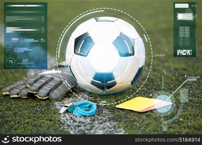 sport, soccer and technology concept - ball, goalkeeper gloves, referee whistle and caution card on football field. ball, gloves, whistle and cards on soccer field