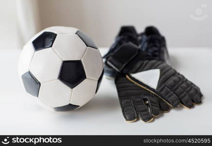 sport, soccer, football and sports equipment concept - close up of ball, boots and goalkeeper gloves on table