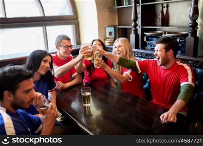 sport, soccer, people and leisure concept - happy friends or football fans clinking beer glasses at bar or pub, supporting two teams with different shirt color