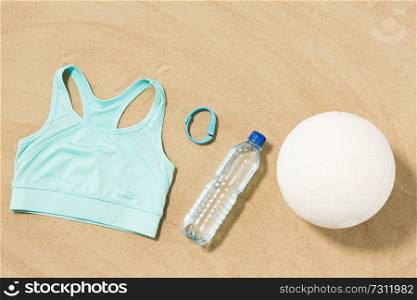 sport, summer and objects concept - sports top, ball, fitness tracker and water bottle on beach sand. sports top, ball, fitness tracker and water bottle