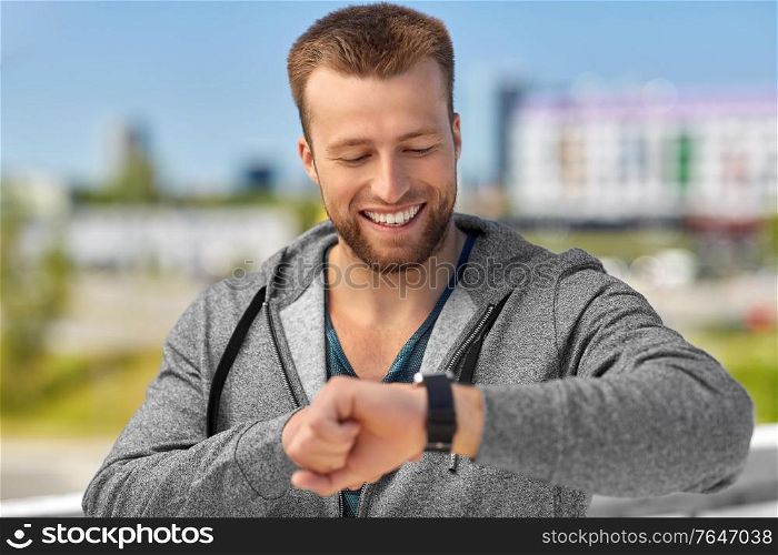 sport, technology and healthy lifestyle concept - happy smiling young man with fitness tracker in city. happy man with fitness tracker in city