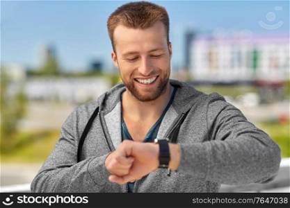 sport, technology and healthy lifestyle concept - happy smiling young man with fitness tracker in city. happy man with fitness tracker in city