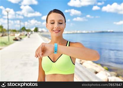 sport, technology and healthy lifestyle concept - happy smiling young woman with fitness tracker on sea promenade. smiling young woman with fitness tracker outdoors