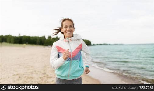 sport, technology and healthy lifestyle concept - smiling woman with fitness tracker running along beach. woman with fitness tracker running along beach