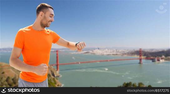 sport, technology and healthy lifestyle concept - smiling young man with smart watch or fitness tracker over golden gate bridge in san francisco bay background. man with fitness tracker over golden gate bridge. man with fitness tracker over golden gate bridge