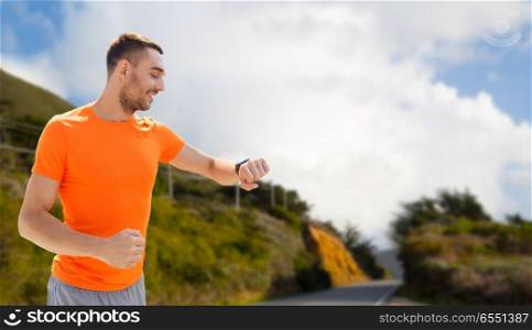 sport, technology and healthy lifestyle concept - smiling young man with smart watch or fitness tracker over big sur hills and road background in california. man with smart watch or fitness tracker. man with smart watch or fitness tracker