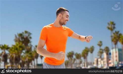 sport, technology and healthy lifestyle concept - smiling young man with smart watch or fitness tracker over venice beach background in california. man with smart watch or fitness tracker. man with smart watch or fitness tracker