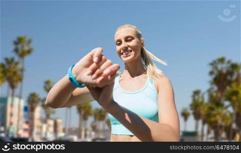 sport, technology and healthy lifestyle concept - smiling young with fitness tracker training over venice beach background in california. woman with fitness tracker exercising outdoors. woman with fitness tracker exercising outdoors