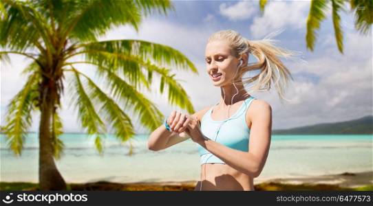 sport, technology and healthy lifestyle concept - smiling young woman with fitness tracker and earphones exercising over tropical beach background in french polynesia. woman with fitness tracker doing sports. woman with fitness tracker doing sports