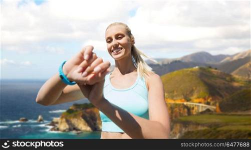 sport, technology and healthy lifestyle concept - smiling young woman with fitness tracker training over big sur hills and pacific ocean background in california. woman with fitness tracker exercising outdoors. woman with fitness tracker exercising outdoors