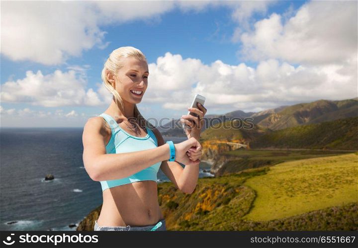 sport, technology and healthy lifestyle concept - smiling young woman with fitness tracker and smartphone exercising over big sur hills and pacific ocean background in california. happy woman with fitness tracker and smartphone. happy woman with fitness tracker and smartphone