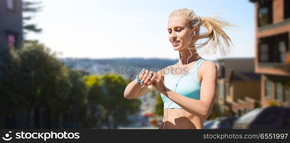 sport, technology and healthy lifestyle concept - smiling young woman with fitness tracker and earphones exercising over san francisco city background. woman with fitness tracker doing sports. woman with fitness tracker doing sports