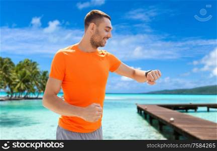 sport, technology and people concept - smiling young man with smart watch or fitness tracker at summer over city street on background. smiling man with smart watch running along beach