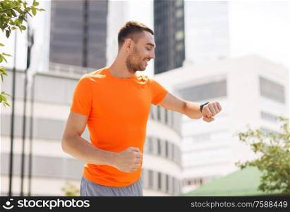 sport, technology and people concept - smiling young man with smart watch or fitness tracker running in summer over city street on background. smiling young man with smart watch running at city